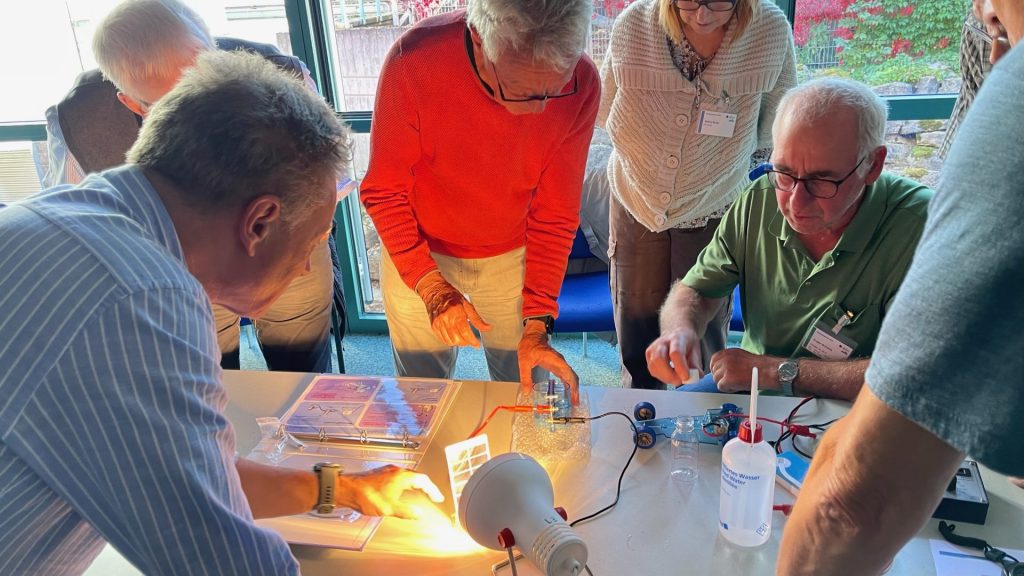 Teilnehmende der Arbeitsgruppe Grüner Wasserstoff stehen um Mini-Elektrolysator zur Inbetriebnahme des Wasserstoffmodellautos